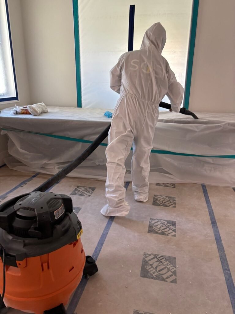 A suited technician vacuuming a room floored with protective paper in the East Bay