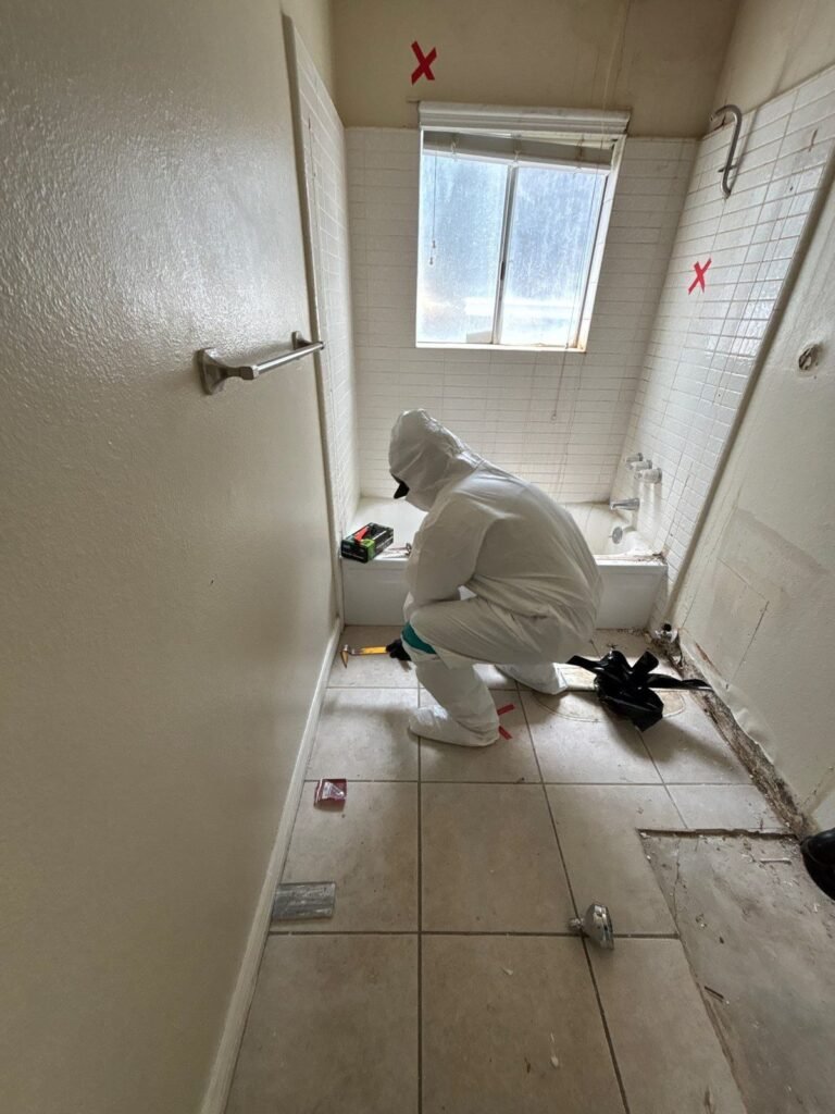 A technician kneeling in a tiled bathroom with red marks showing where the wall gets cut in the East Bay