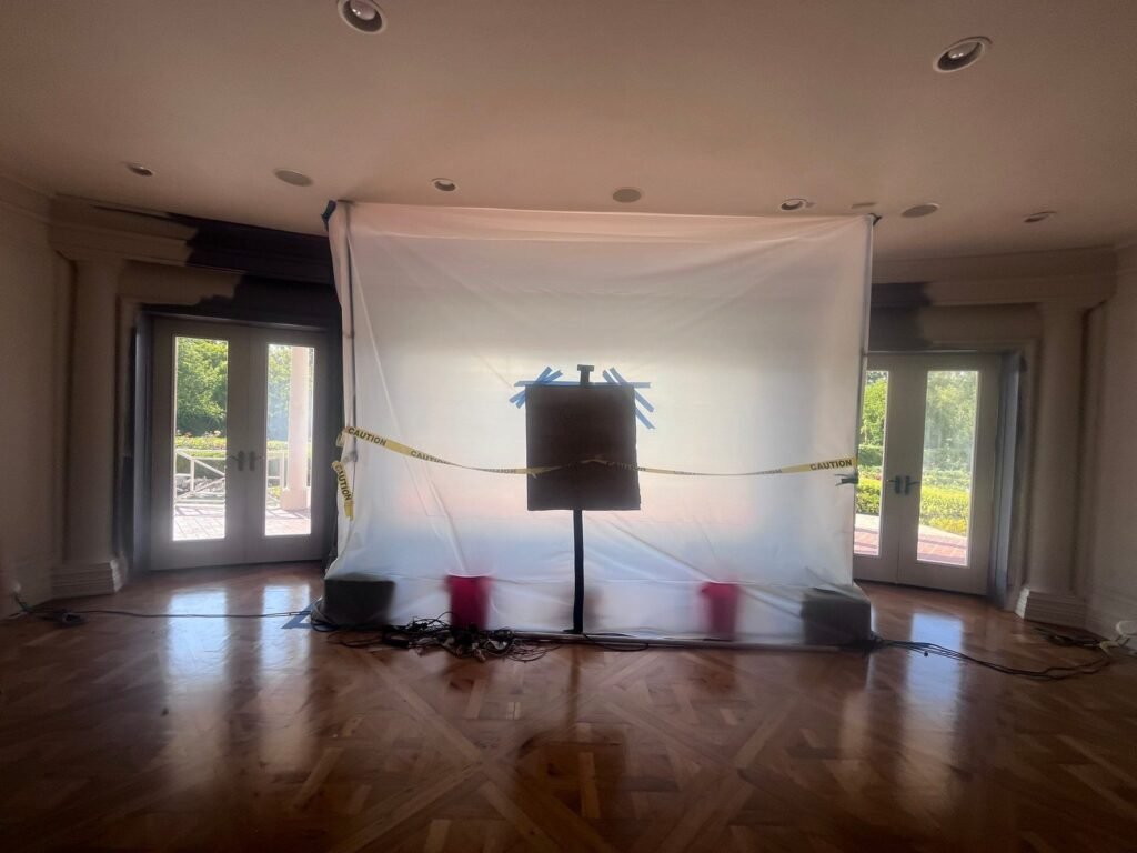 A cleared living room with hardwood floors and a plastic containment wall at the far end in the East Bay