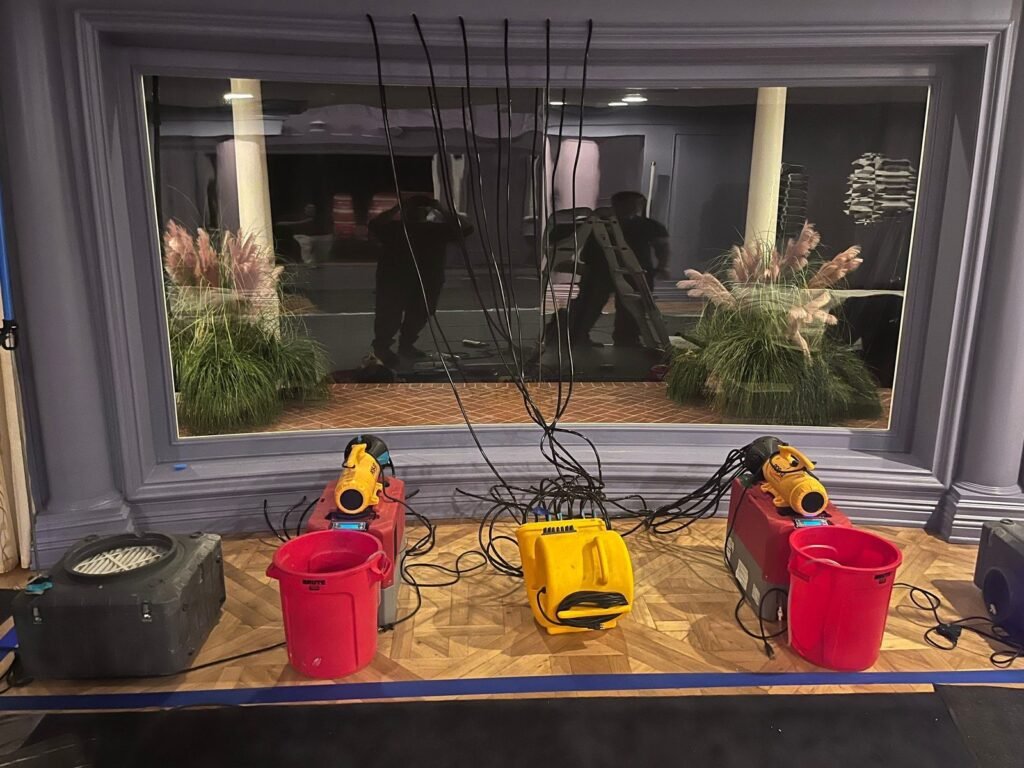 Two yellow air movers and red dehumidifiers lined up under a bay window in the East Bay