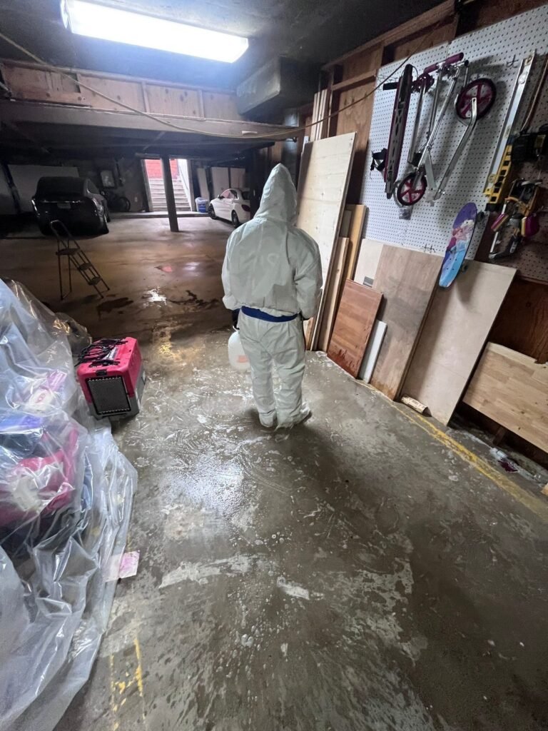 A technician in a garage with a wet floor and stored contents stacked to one side in the East Bay