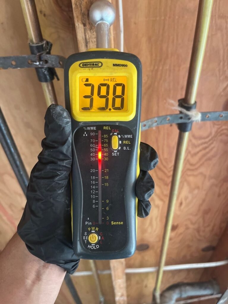 A moisture meter reading 39.8 against plywood sheathing in the East Bay