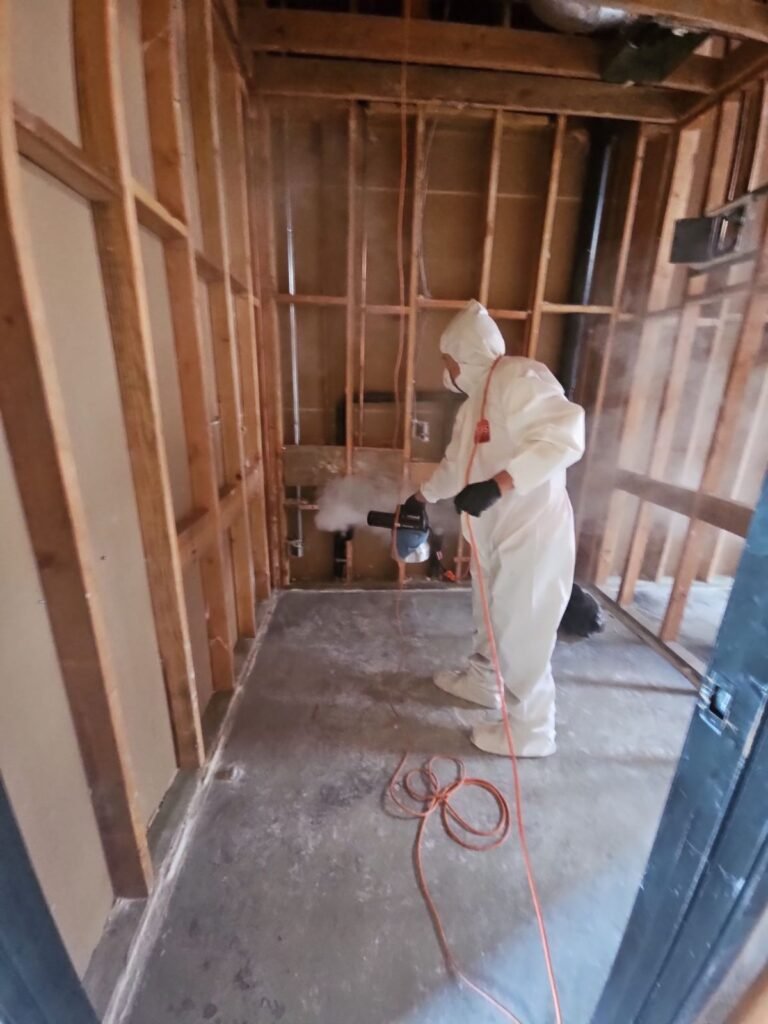 A technician spraying in a room stripped to the studs over bare concrete in the East Bay