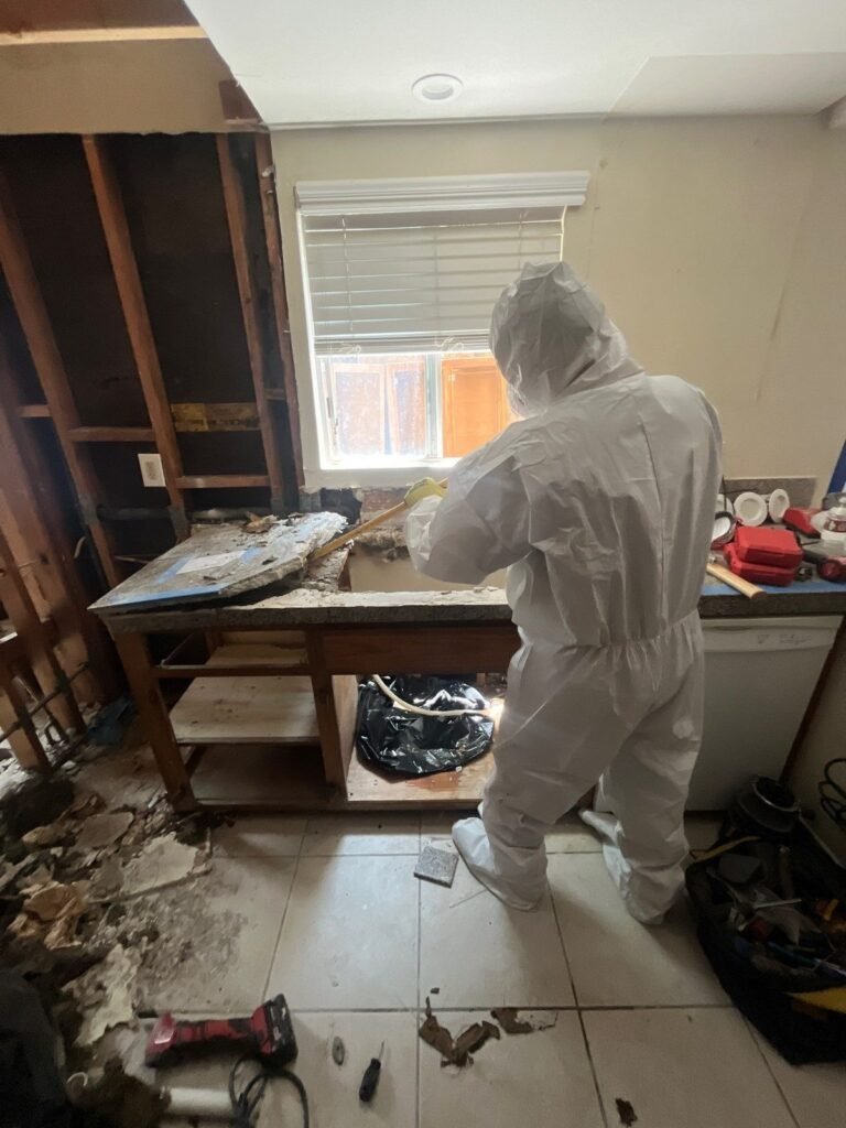 A suited technician lifting ruined material out of a demolished kitchen in the East Bay