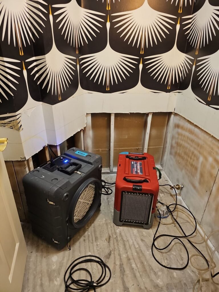 An air scrubber and dehumidifier running in a room with patterned wallpaper and the wall cut at the base in the East Bay