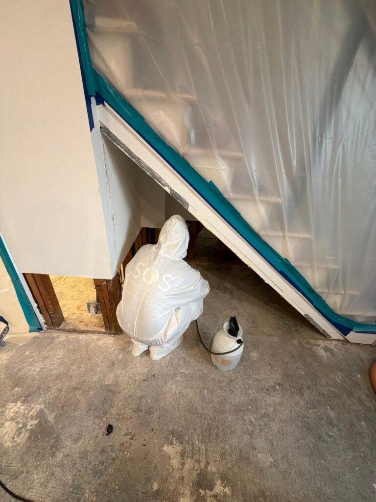 A suited technician working under a plastic barrier on bare concrete in the East Bay