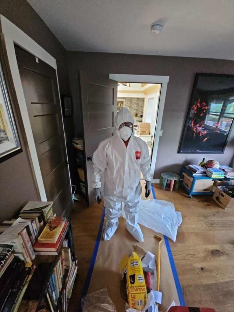 A suited technician working in a lived-in living room with bookshelves and taped floor protection in the East Bay
